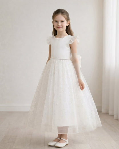 Front view of a junior flower girl wearing an ivory white A-line formal dress with a pearl neckline and sparkly tulle skirt.