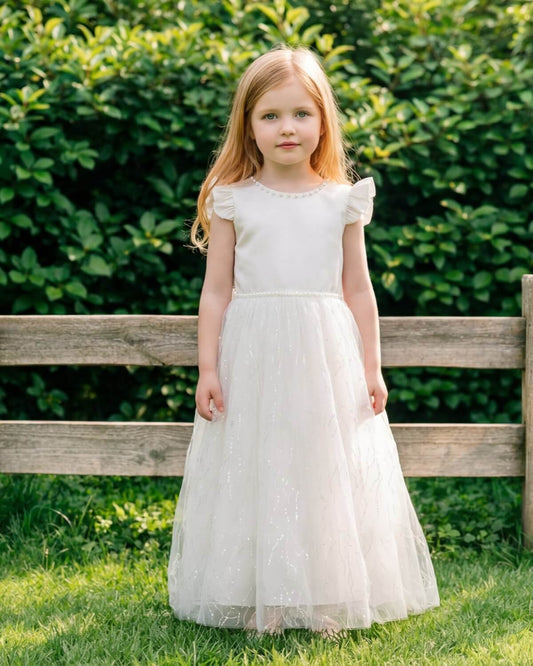 Close-up portrait of a happy flower girl looking up, highlighting the pearl neckline and ruffled flutter sleeves of her ivory dress.