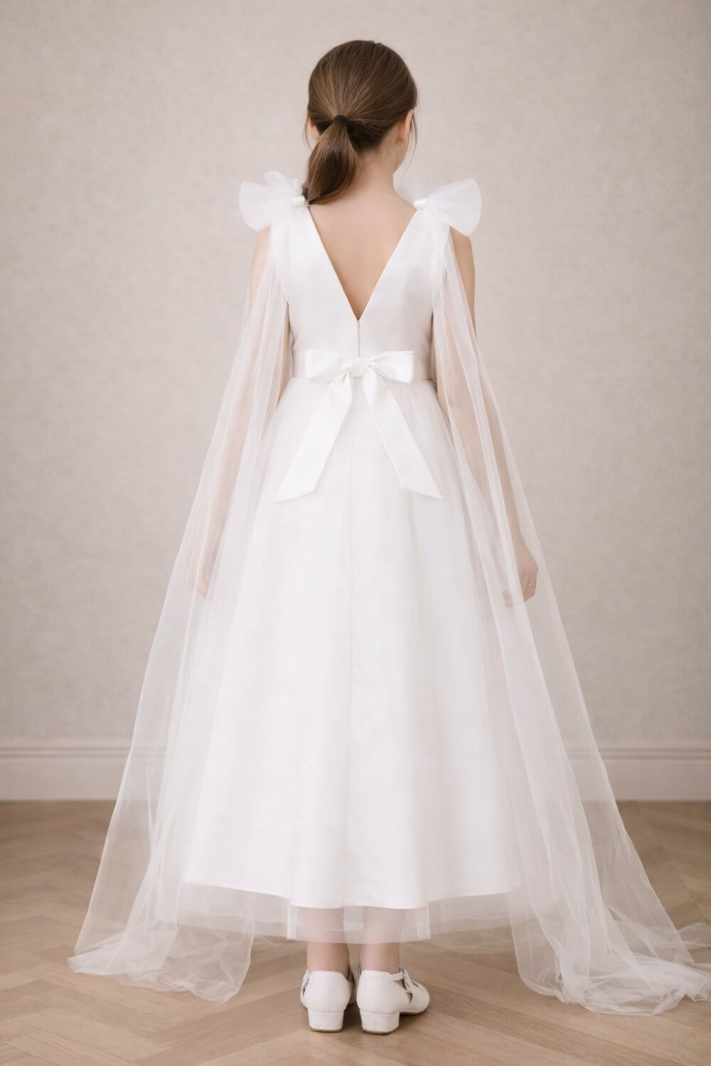 Back view of an elegant ivory white flower girl dress showcasing a deep V-back, a classic satin bow, and whimsical tulle shoulder wings.