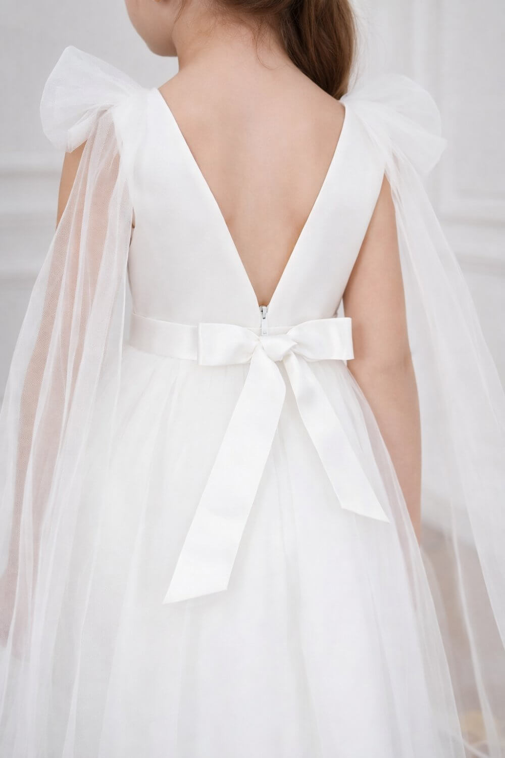 Macro shot showing the craftsmanship of the deep V-back, hidden zipper, and secure satin bow on the Aria flower girl gown.