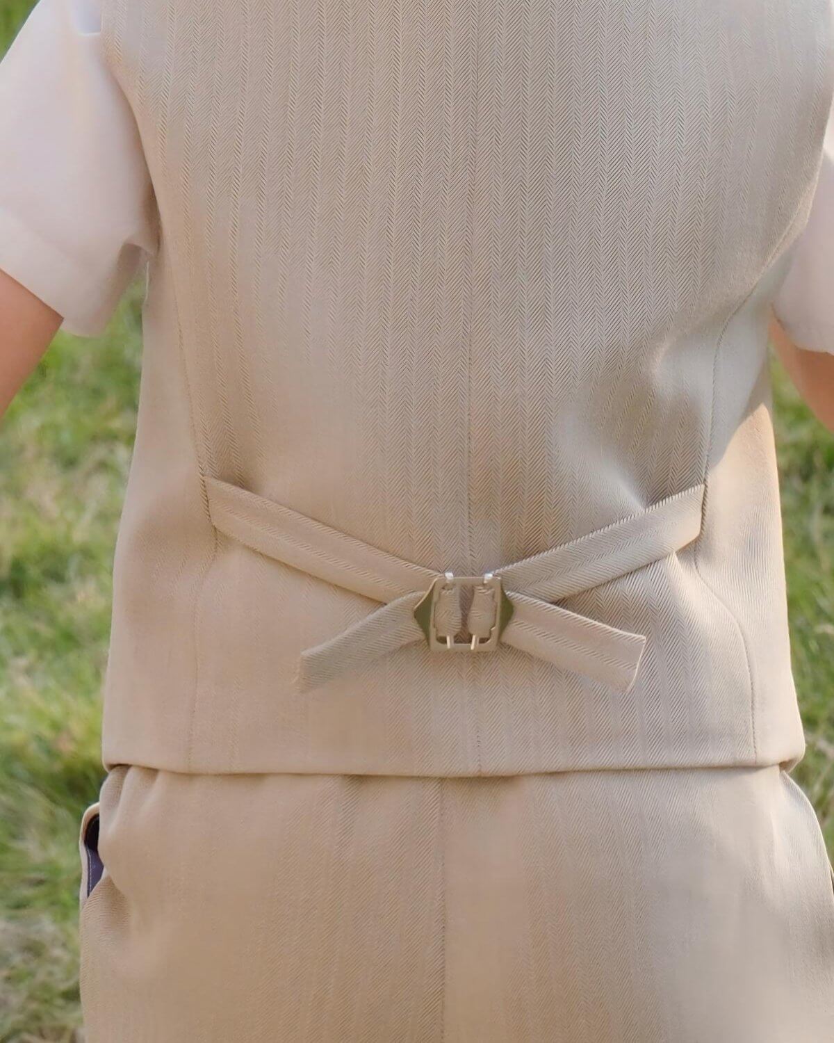 Back view detail of boys khaki linen formal vest showing the adjustable metal buckle strap and herringbone weave pattern