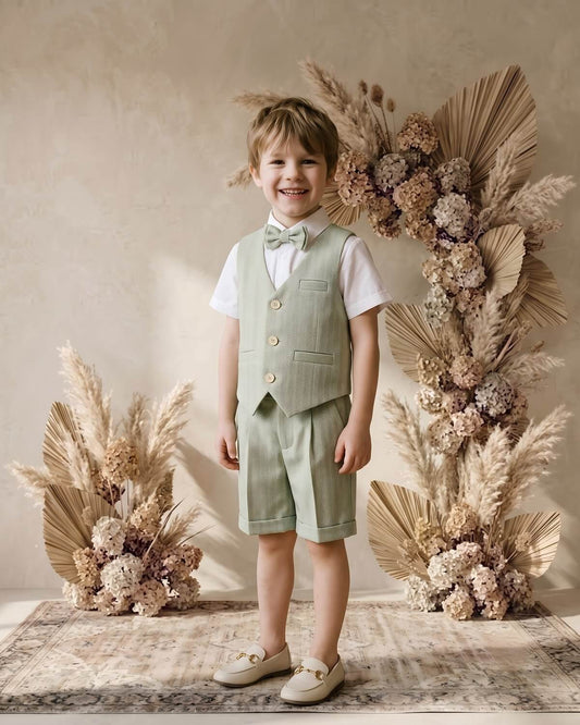 Smiling young boy wearing a sage green herringbone vest and shorts suit set for summer weddings.