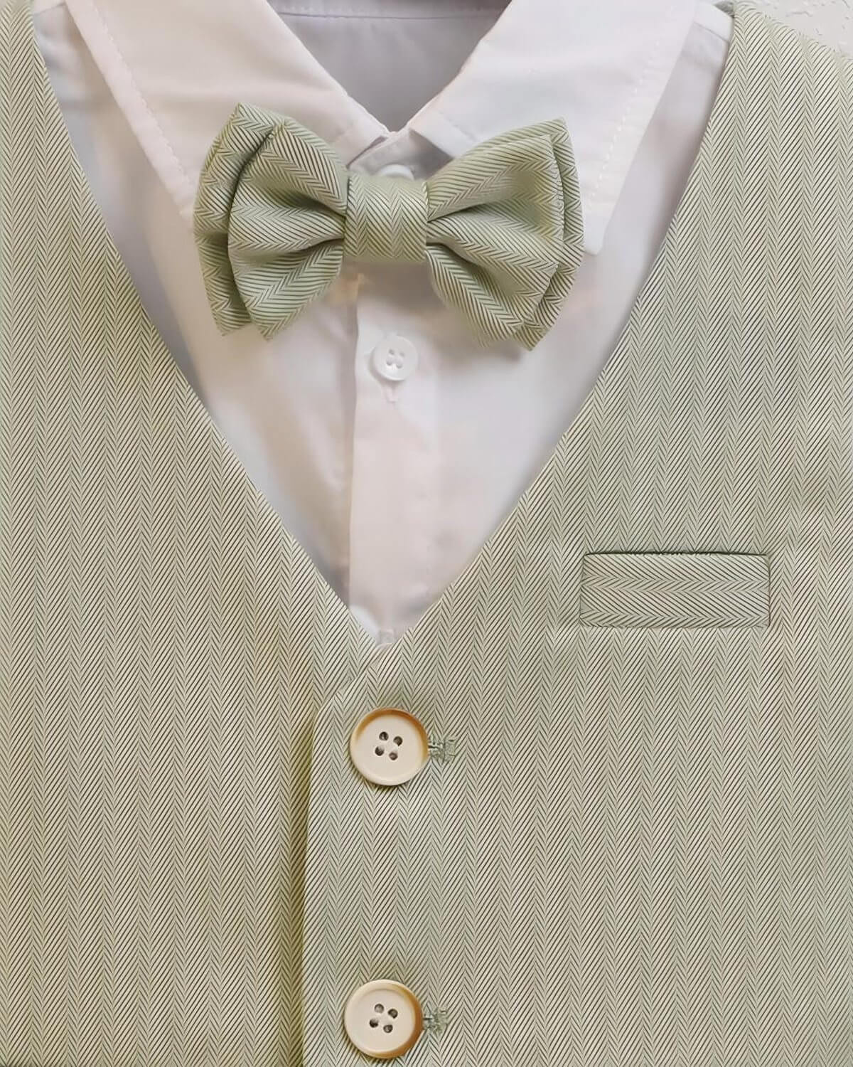 Close-up of matching sage green herringbone bow tie and crisp white dress shirt collar.
