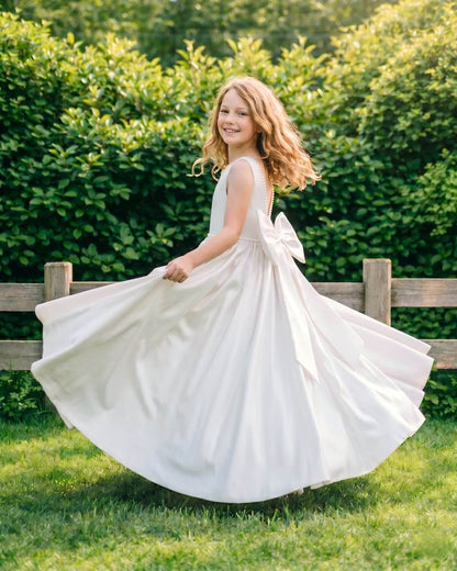 Little Ivory The Grace satin wedding flower girl dress twirling in a green grass field showing full A line skirt