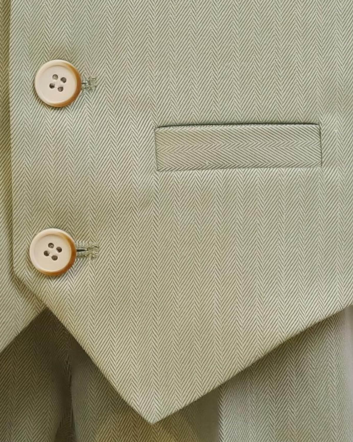 Macro shot of premium sage green herringbone fabric, featuring tailored faux pocket and vintage-style buttons.