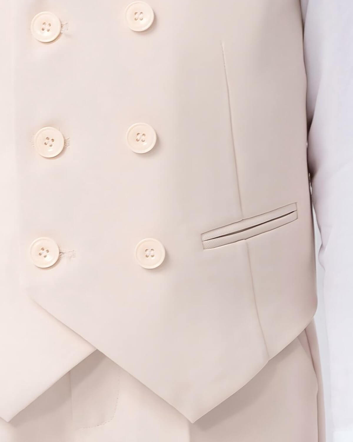 Macro close-up of the elegant 6-button layout and pocket welt detail on a boys oatmeal double-breasted waistcoat.