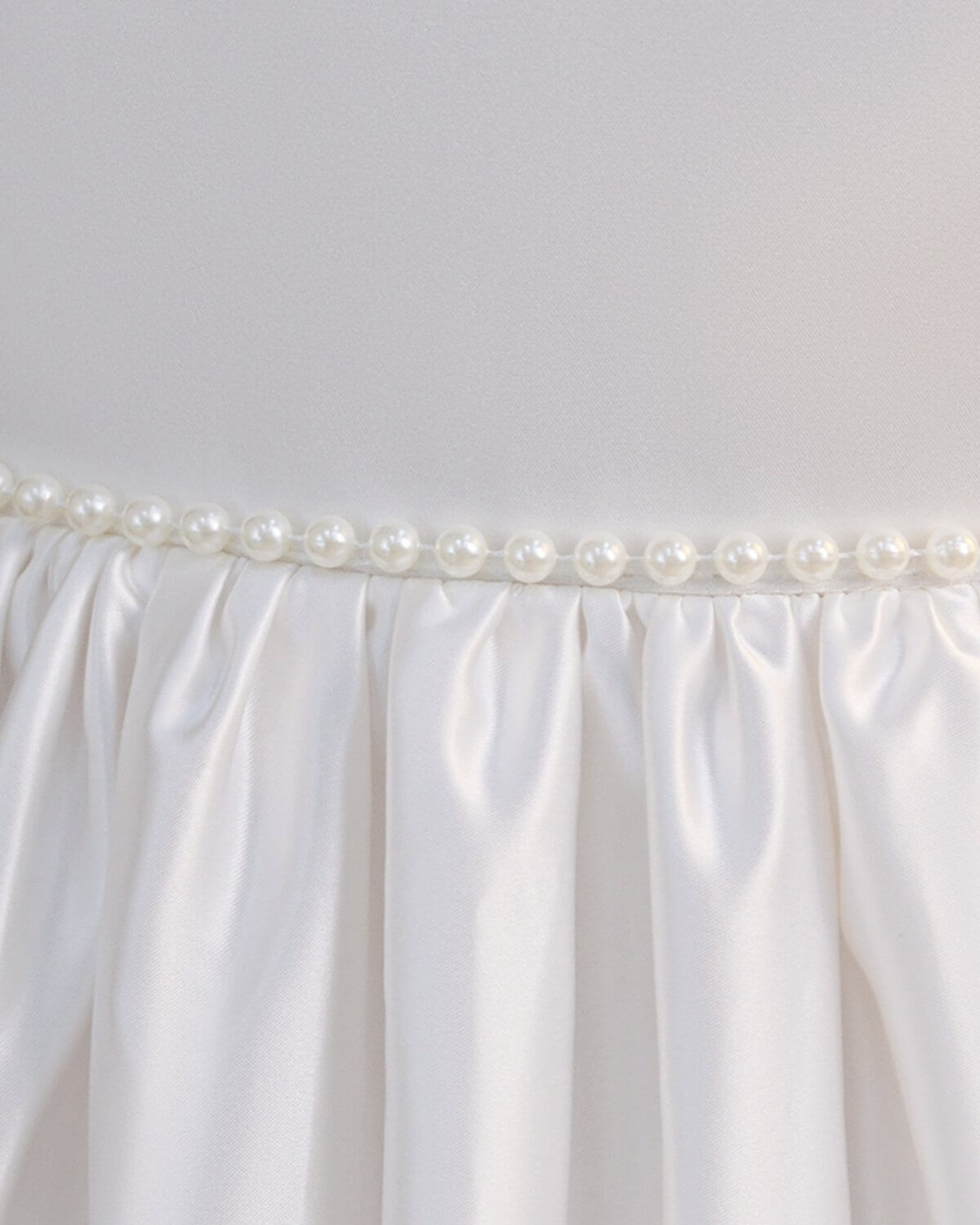 Detail shot of luxury pearl trim waistline and neat pleats on The Grace ivory satin flower girl dress