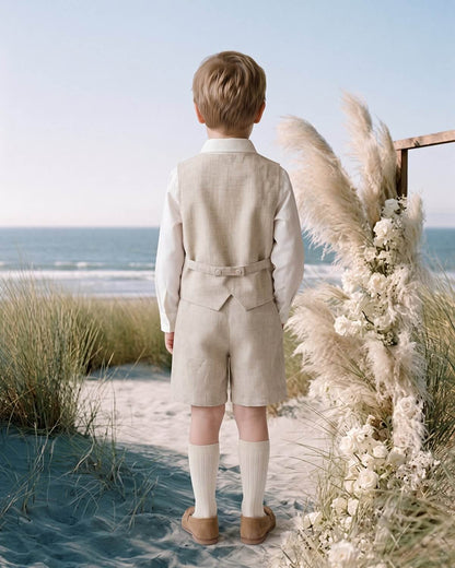 Studio back view of a boy wearing an oatmeal linen-lyocell vest and Bermuda shorts set with adjustable back buckle.