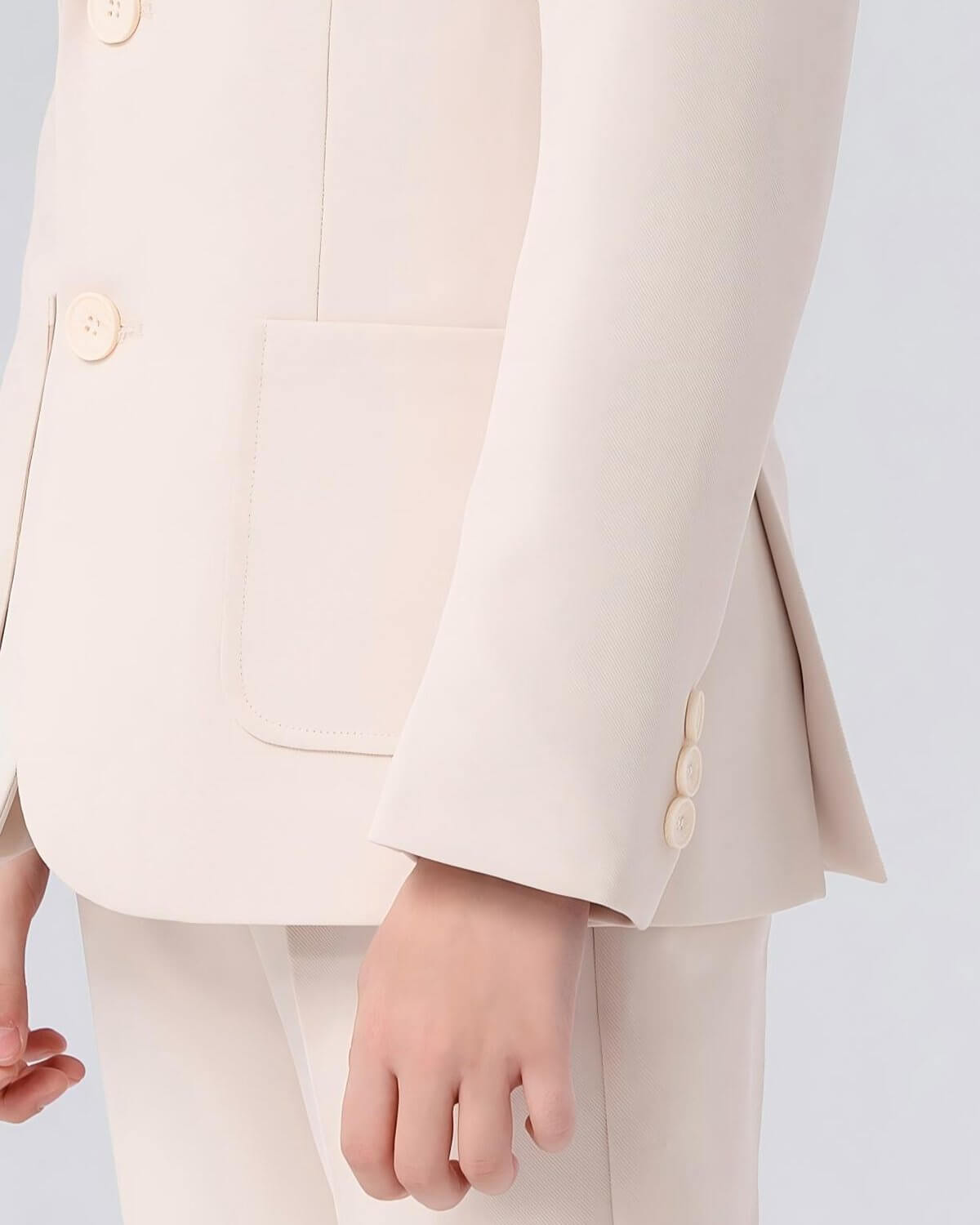Close-up detail of the sleeve buttons and flap pocket on a boys beige suit jacket.
