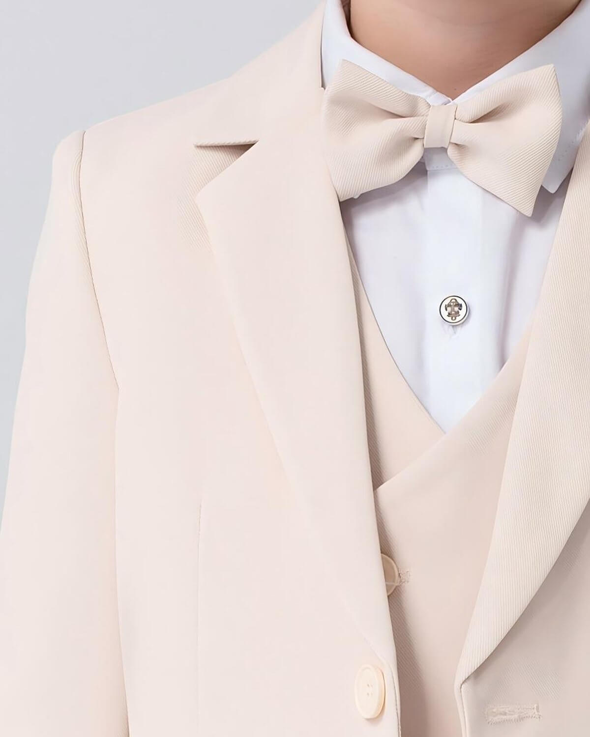 Close-up of the lapel, matching vest, and pre-tied bow tie of a boys beige formal suit.