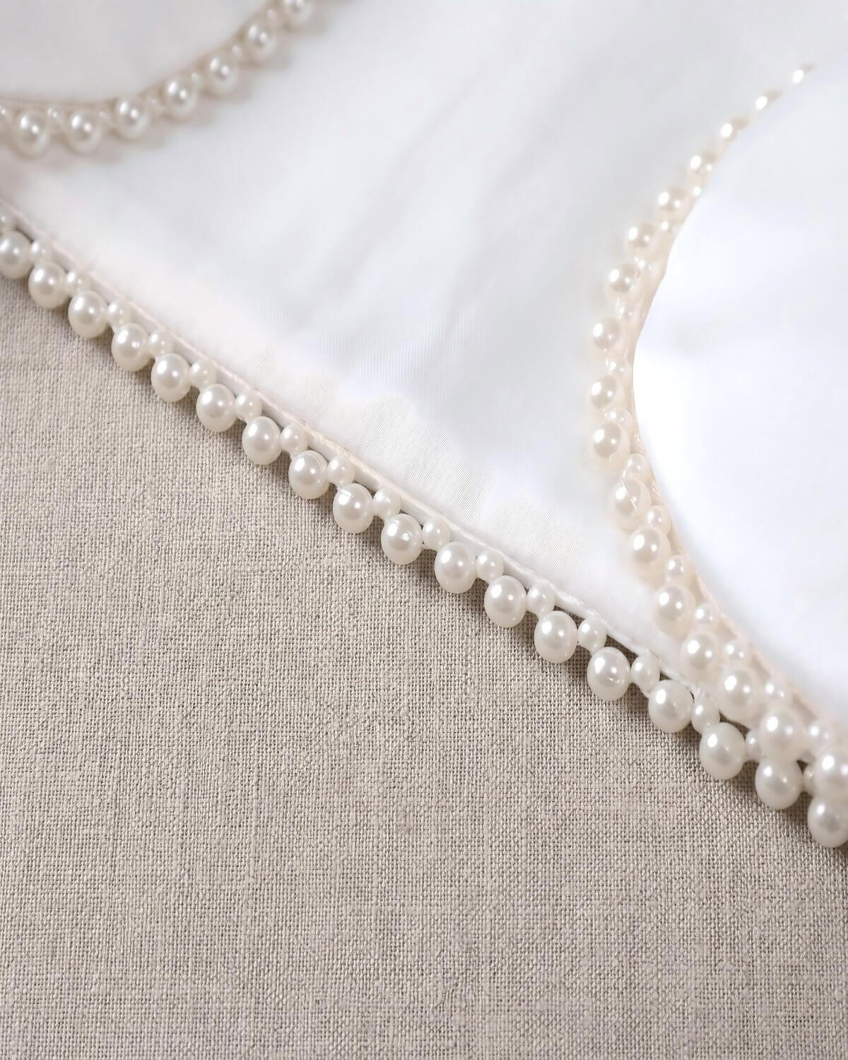 Macro close-up shot of the exquisite hand-stitched pearl beads lining the edge of the smooth white matte satin formal jacket.