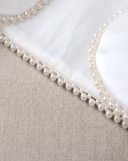Macro close-up shot of the exquisite hand-stitched pearl beads lining the edge of the smooth white matte satin formal jacket.