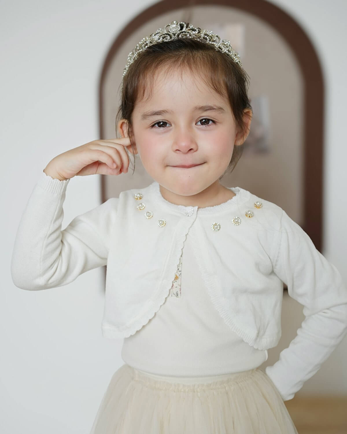 Little girl with a crystal tiara wearing a cropped white cotton knitted shrug cardigan, perfect for a Holy Communion or flower girl dress accessory.