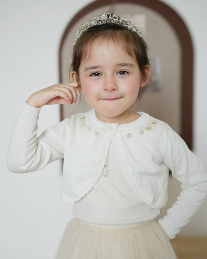 Little girl with a crystal tiara wearing a cropped white cotton knitted shrug cardigan, perfect for a Holy Communion or flower girl dress accessory.