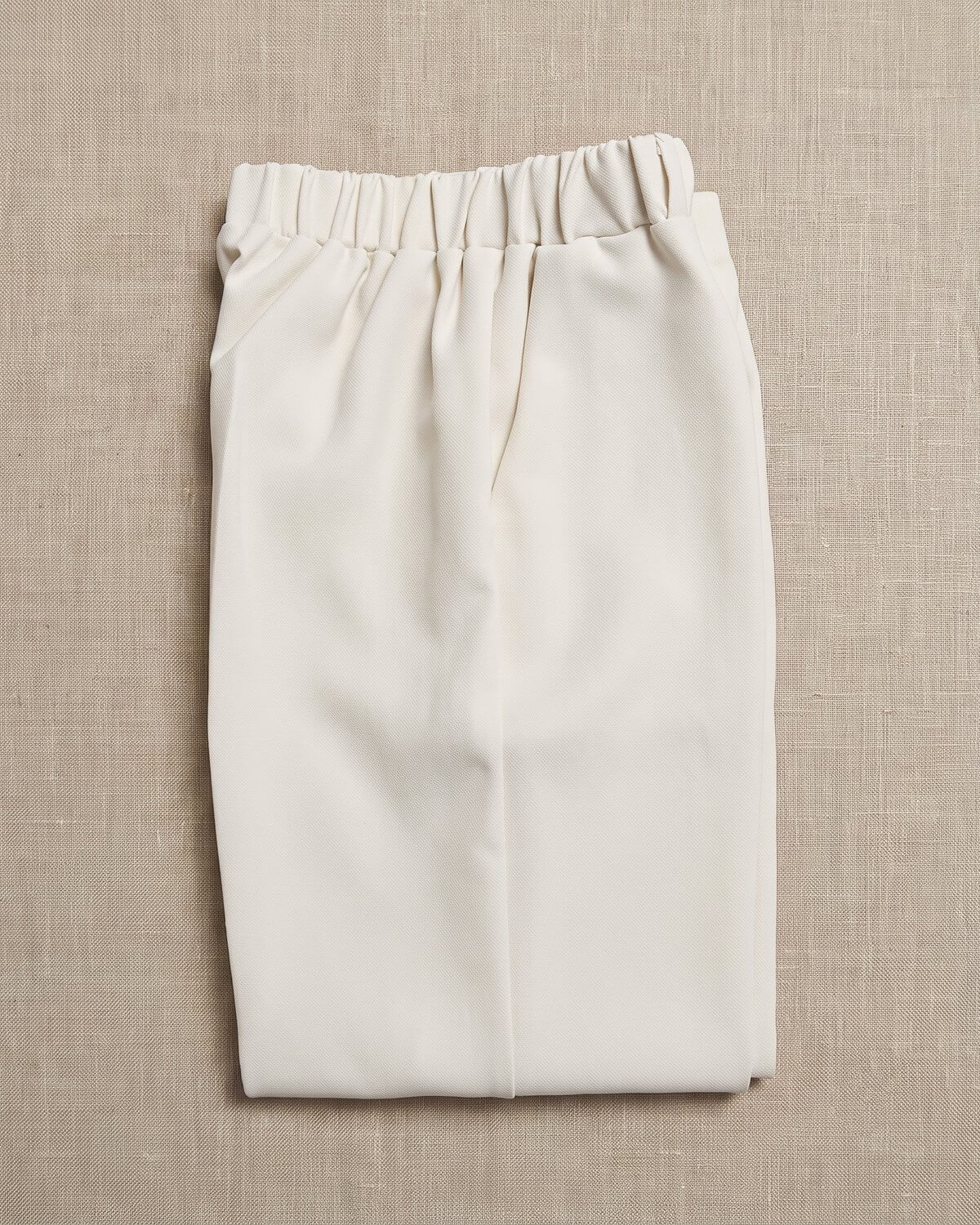 Little Ivory boy's formal beige cream wedding suit trousers waistband detail. Close-up showing the comfortable elastic waistband, crisp front crease, and soft cream linen fabric texture.