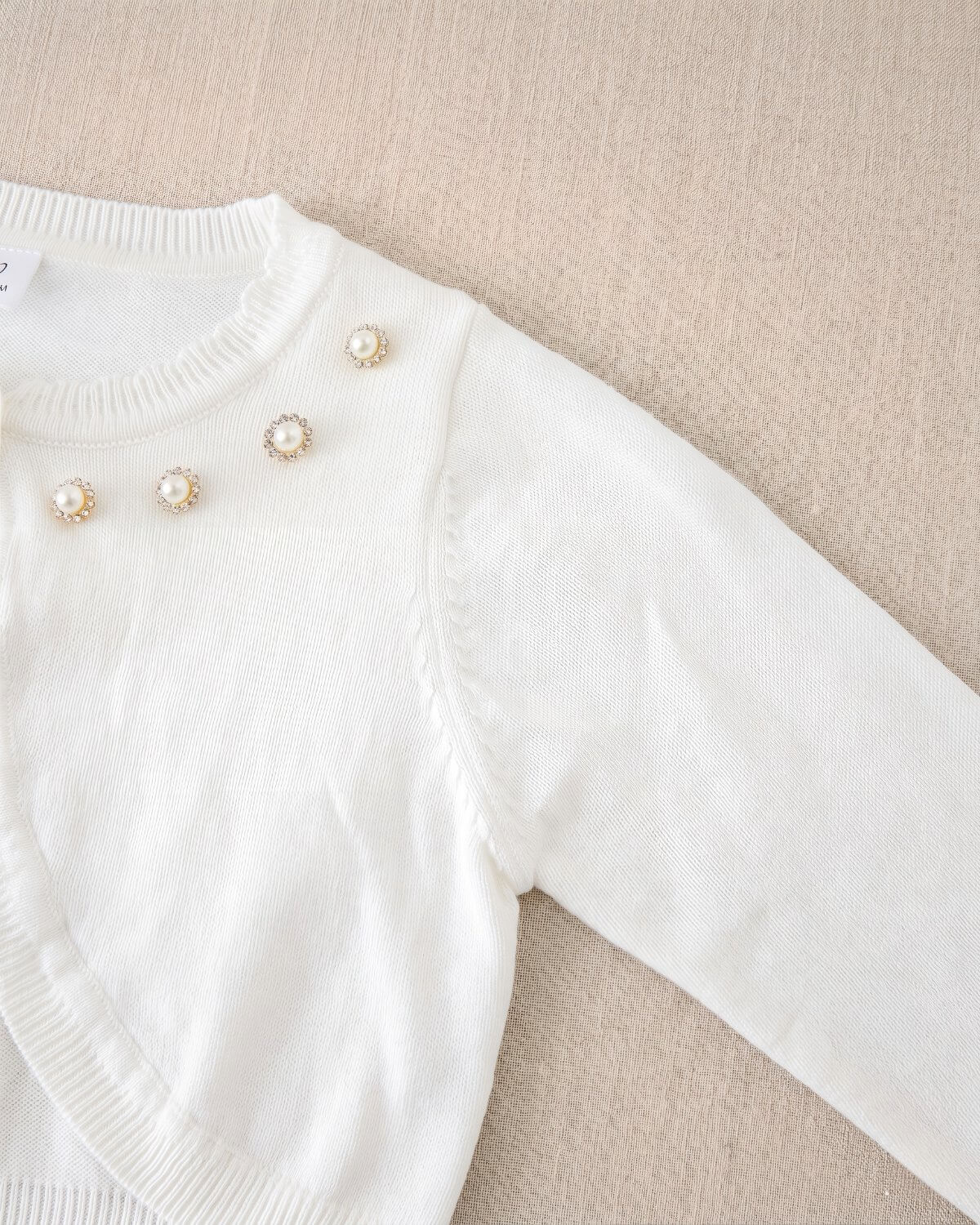 Macro flat-lay view of the seamless shoulder construction and tight knit texture of the white formal girls sweater cardigan.