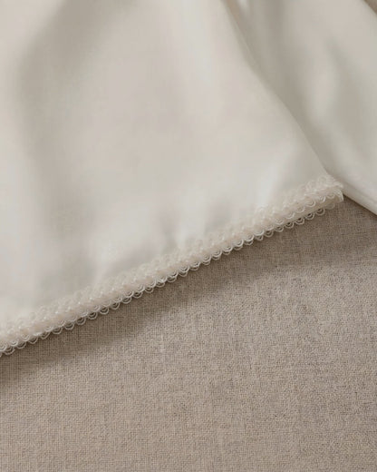 Macro close-up shot of the exquisite hand-crafted pearl beaded scalloped lace trim lining the bottom edge of the smooth ivory satin jacket.