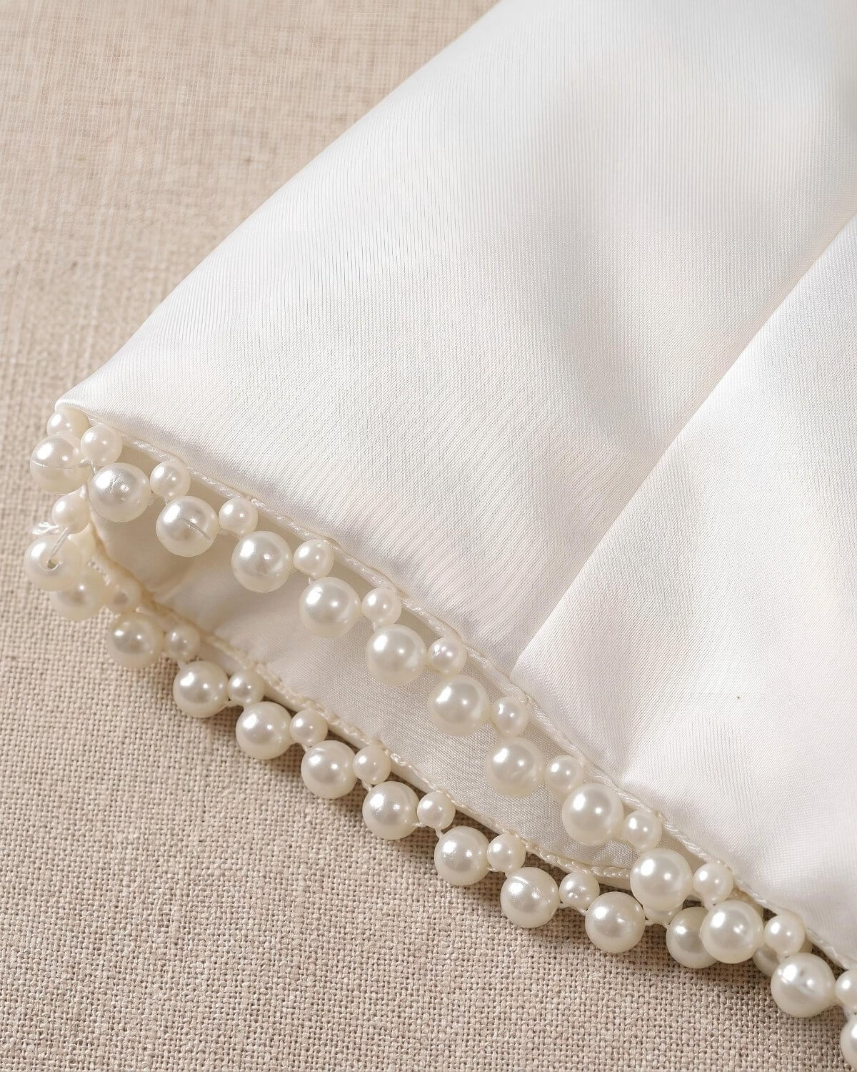 Flat lay view of the premium fine-woven matte satin fabric and luxury pearl trim on the sleeve cuff of a girls formal dress cardigan.