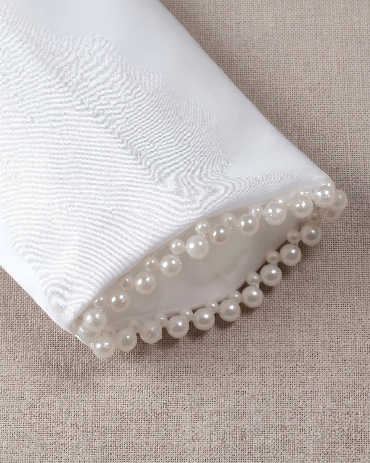 Detailed texture view of the long sleeve cuffs on the kids white satin bolero showing high-end double-row pearl bead embroidery details.
