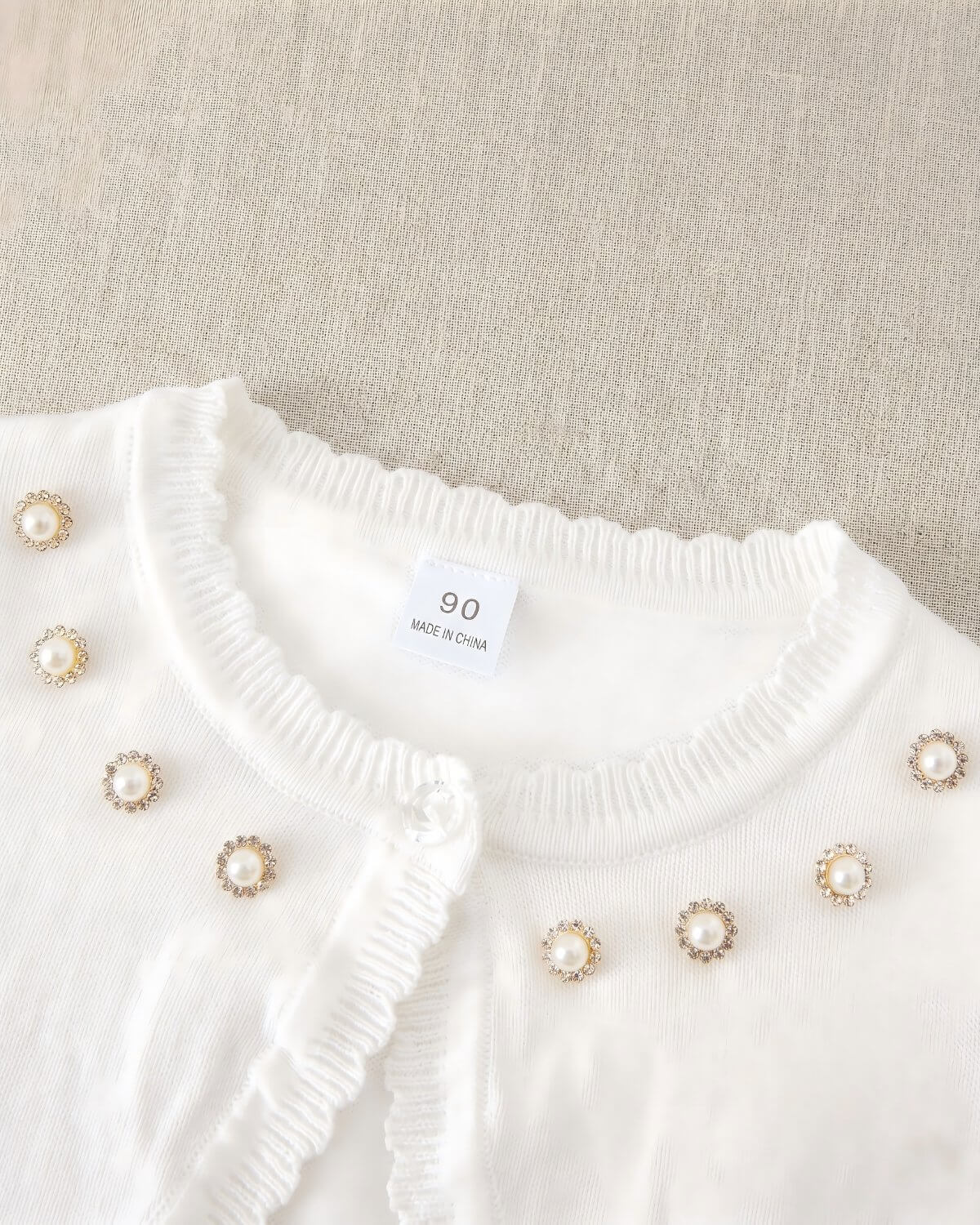 Close-up of the formal kids cardigan collar featuring luxury hand-placed rhinestone pearl halos, clear crystal button, and size 90 garment tag.